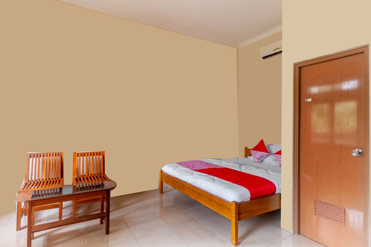 Una camera da letto con un letto, due sedie di legno, un tavolo in legno e una porta.