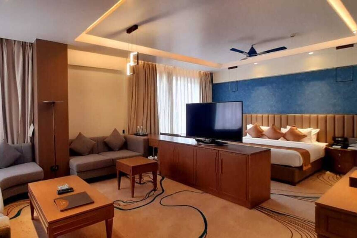 A modern hotel room with a sofa, a bed, a television, and a desk.