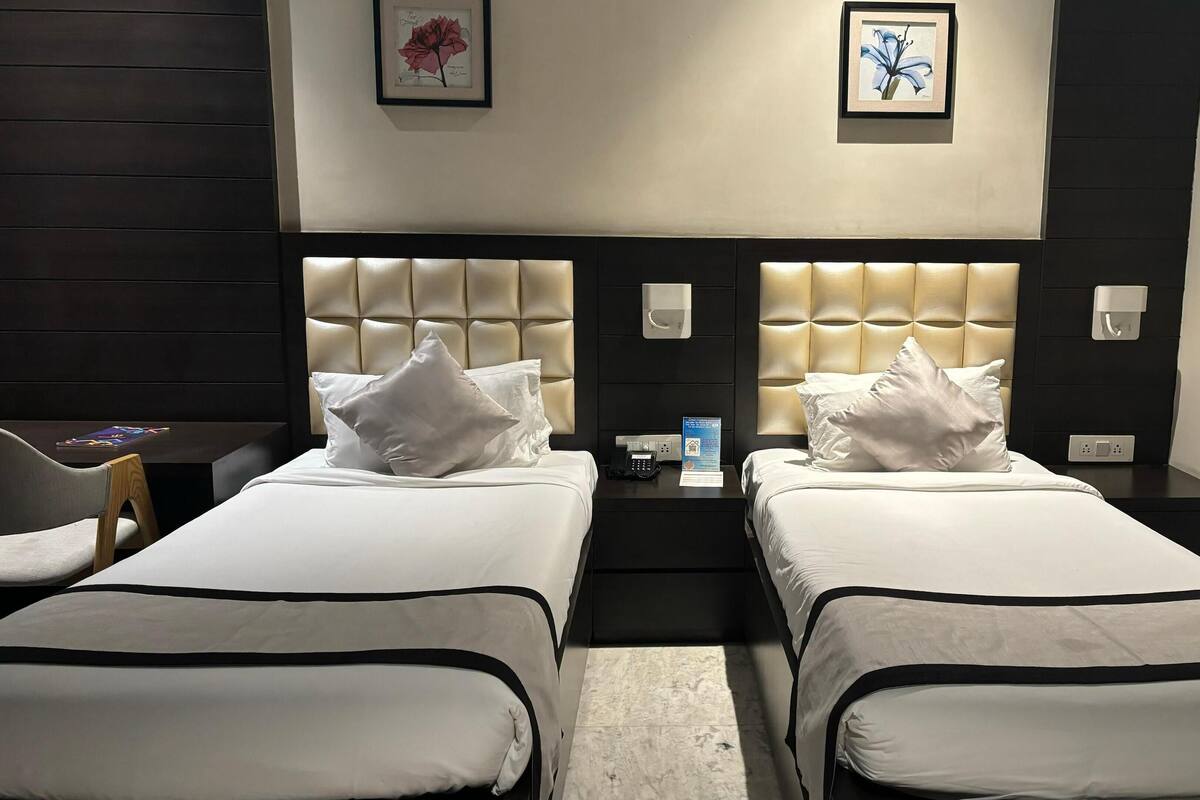 A hotel room with two beds, each with a headboard, a bedside table, and a chair.
