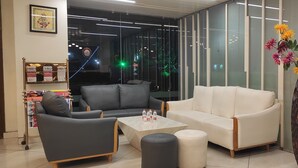 A modern lobby with a grey sofa, a white sofa, a marble coffee table, and a decorative vase with flowers. - Wonder Country Club and Resort (Kharagpur)