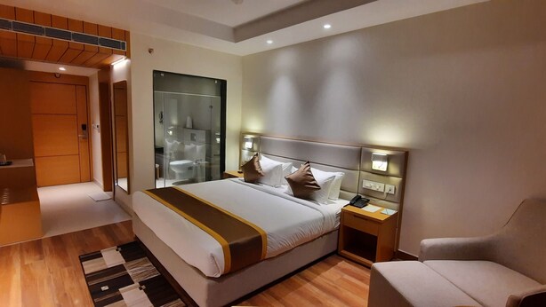 A modern hotel room with a large bed, bedside tables, a chair, and a walk-in closet. - Wonder Country Club and Resort (Kharagpur)