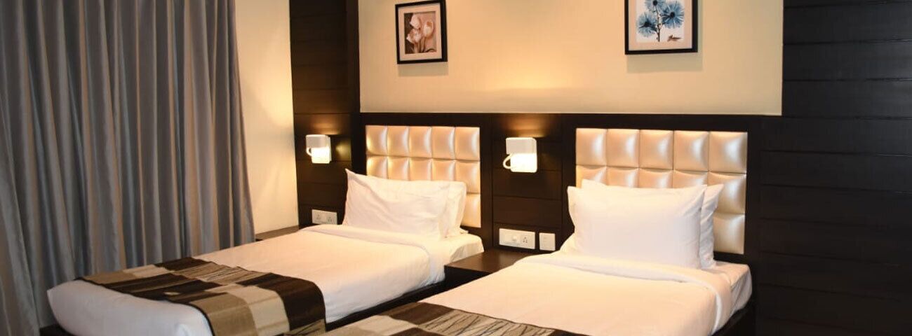 A hotel room with two beds, each with a headboard, bedside lamps, and a window with curtains.