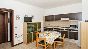 A compact kitchen with a dining table, chairs, a cabinet with glass doors, a stove, and a microwave.