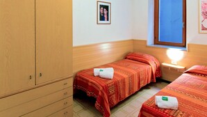 A room with two beds, a wooden wardrobe, a small bedside table with a lamp, and a framed picture on the wall. - Lovely apartment for 5 people with WIFI, A/C, pool, TV and terrace (Torri Del Benaco)