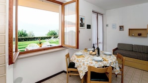 A dining area with a table set for two, a window with an open shutter, a sofa, and a small shelf with items. - Lovely apartment for 5 people with WIFI, A/C, pool, TV and terrace (Torri Del Benaco)