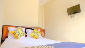 Habitación de hotel con cama, dos almohadas con diseño azul y amarillo, televisor de pantalla plana montado en la pared y cabecero de madera.