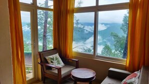 A room with a large window, a wooden chair, a small round table, and a sofa. - Azalea (Narendranagar)