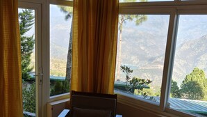 A room with a view of a mountainous landscape through large windows, a chair with a cushion, and yellow curtains. - Azalea (Narendranagar)