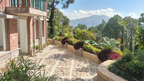 A building with a tiled patio, a balcony with green railings, and a view of a mountainous landscape. - Azalea (Narendranagar)