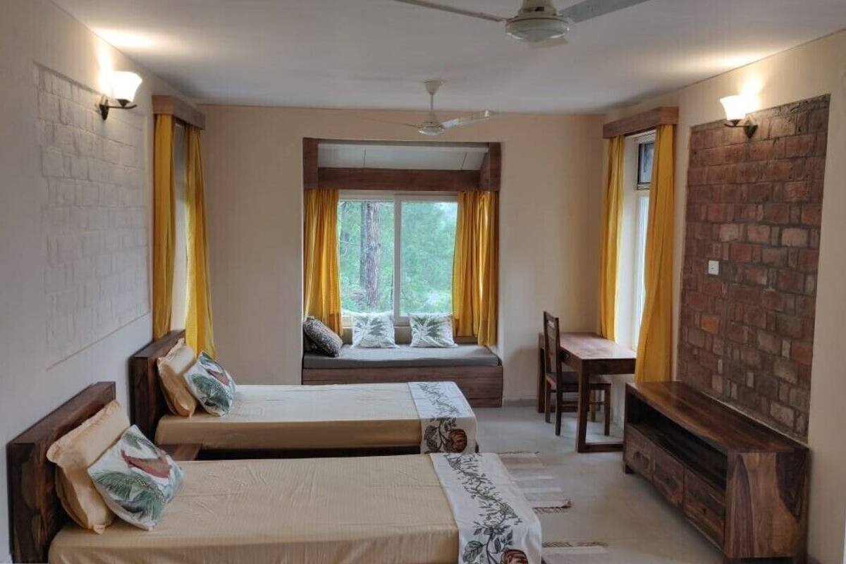 A room with two beds, a bench, a table, a fireplace, and a view of trees.