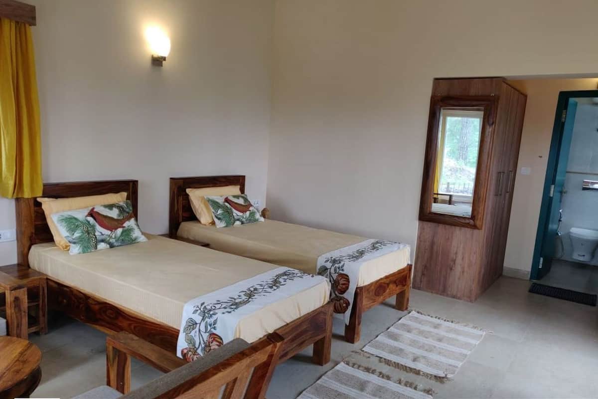 A room with two wooden beds, a small wooden table, a window with a view, and a bathroom door.