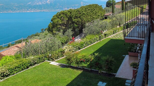 Un balcón con vistas a un jardín cuidado y un paisaje costero.