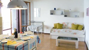 Una sala de estar con un sofá, una mesa de comedor con sillas, una mesa auxiliar y una lámpara.