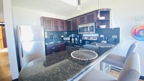 A modern kitchen with dark wooden cabinets, stainless steel appliances, and a black granite countertop.