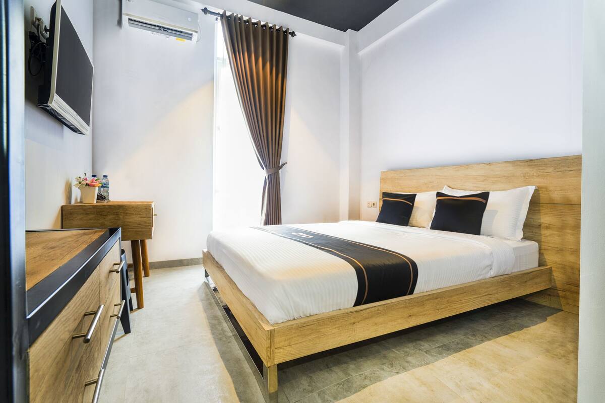 A modern hotel room with a wooden bed, a wooden dresser, a flat-screen TV, and a large window with curtains.