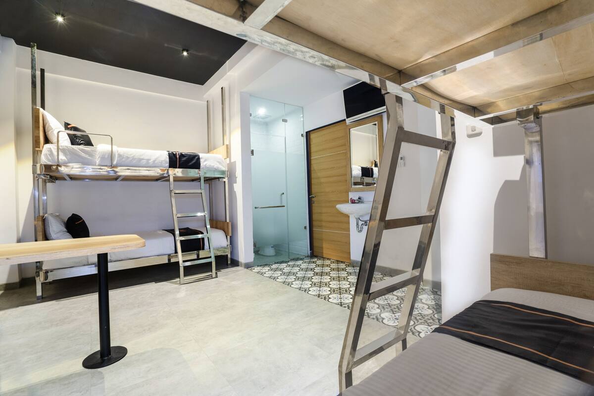 A compact hotel room with a bunk bed, a desk, and a ladder.