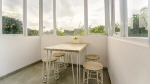 A corner room with a wooden table and four stools, large windows, and a view of greenery outside.