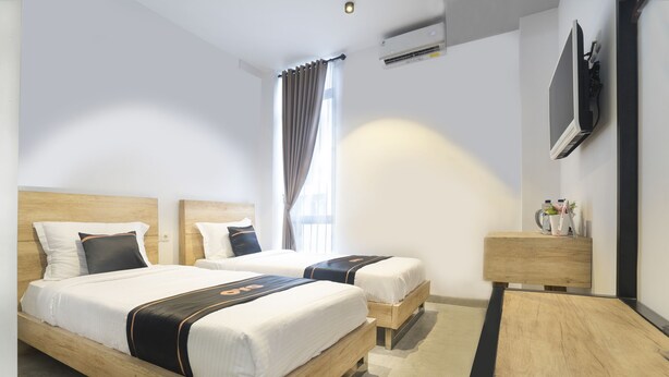 A hotel room with two beds, a TV, a bedside table, and a window with curtains.