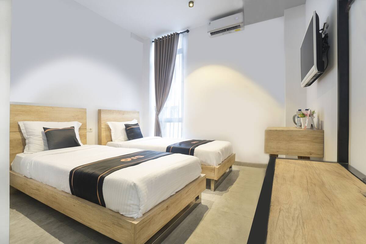 A hotel room with two beds, a TV, a bedside table, and a window with curtains.