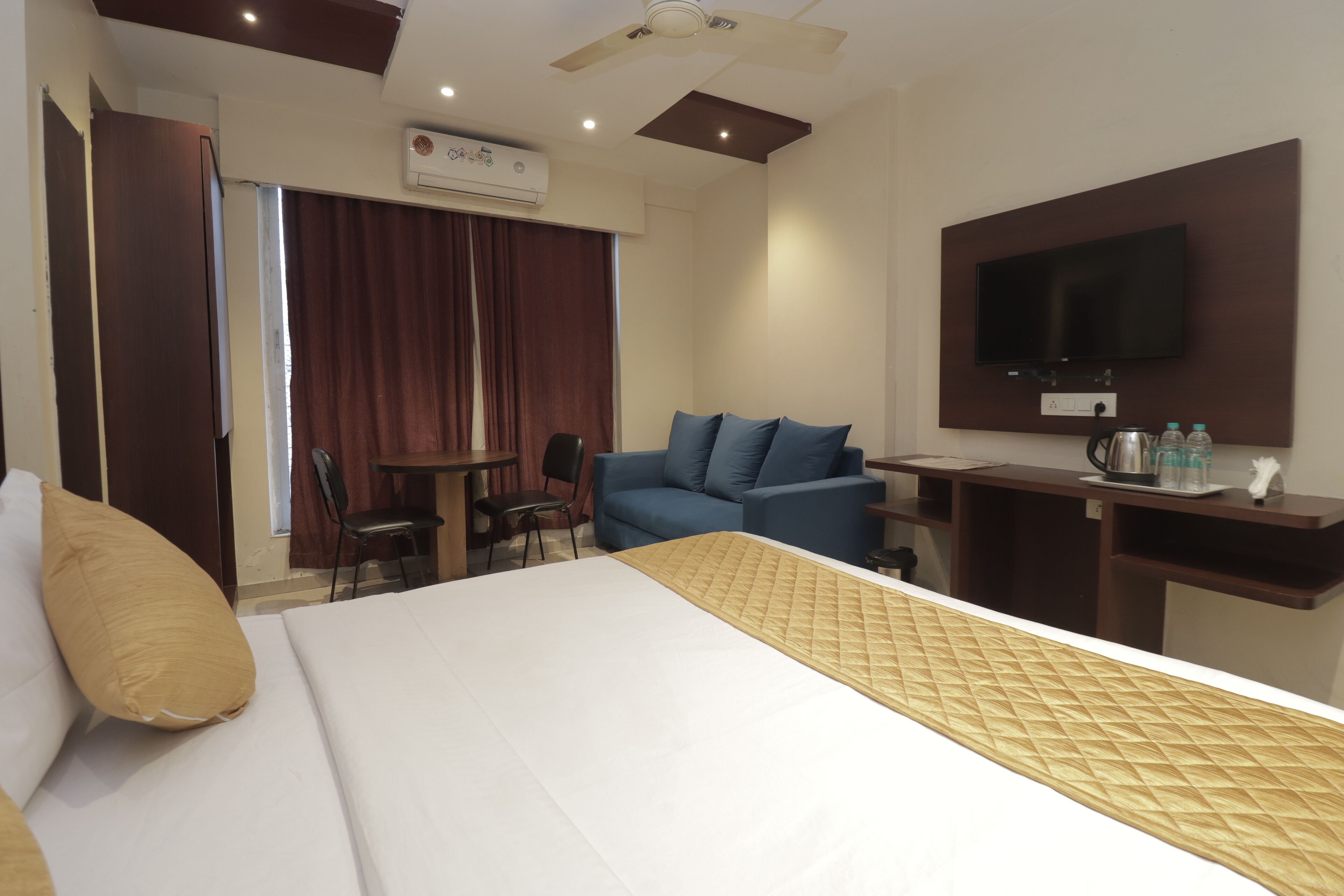 A hotel room with a bed, a sofa, a desk, a television, and an air conditioning unit.