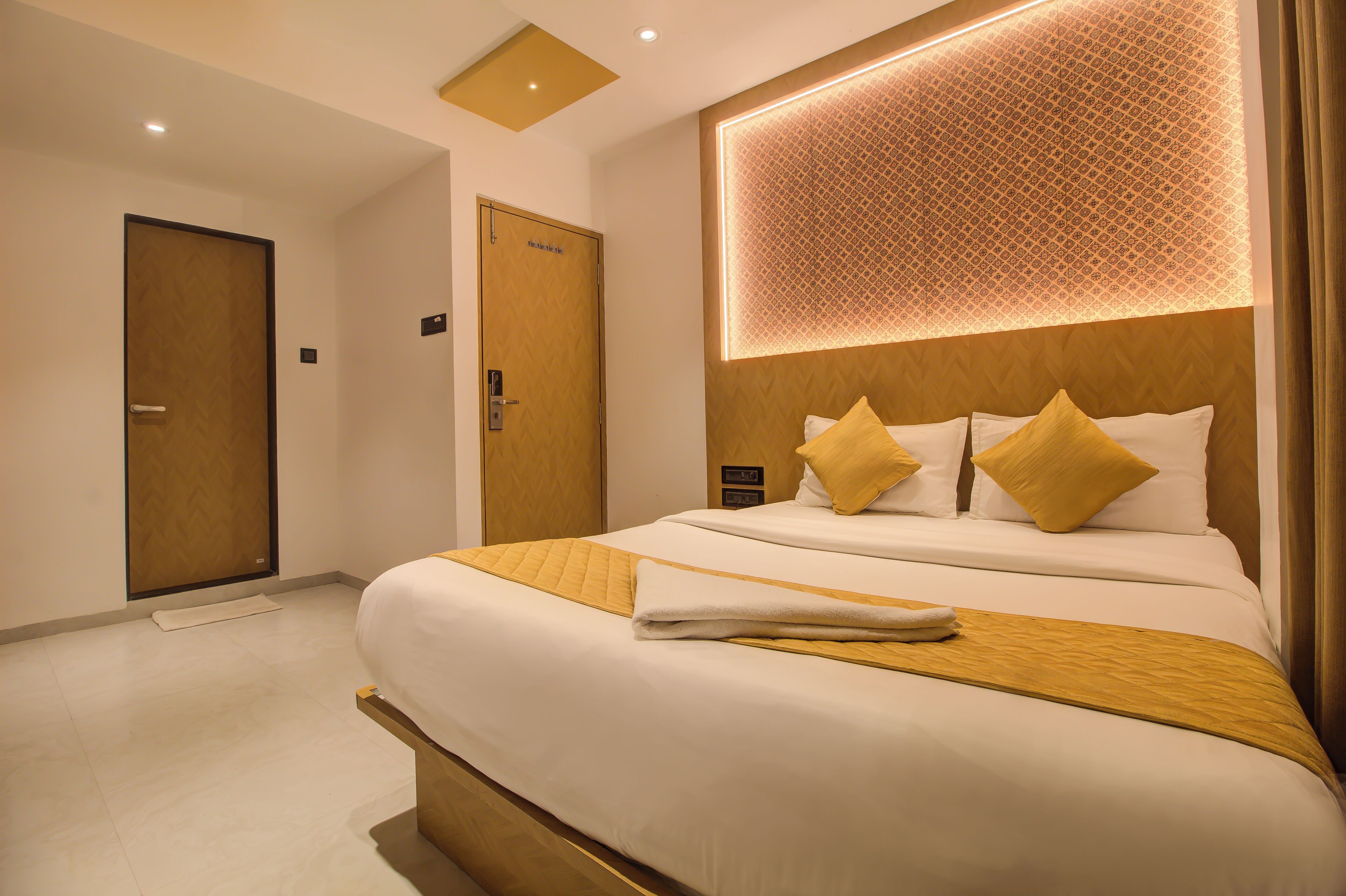A hotel room with a large bed, a wooden headboard, and a patterned wall design.
