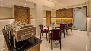 A buffet area with a self-service station, a table with bottled water, and a seating area with chairs. - Hotel Malad Inn (Mumbai)