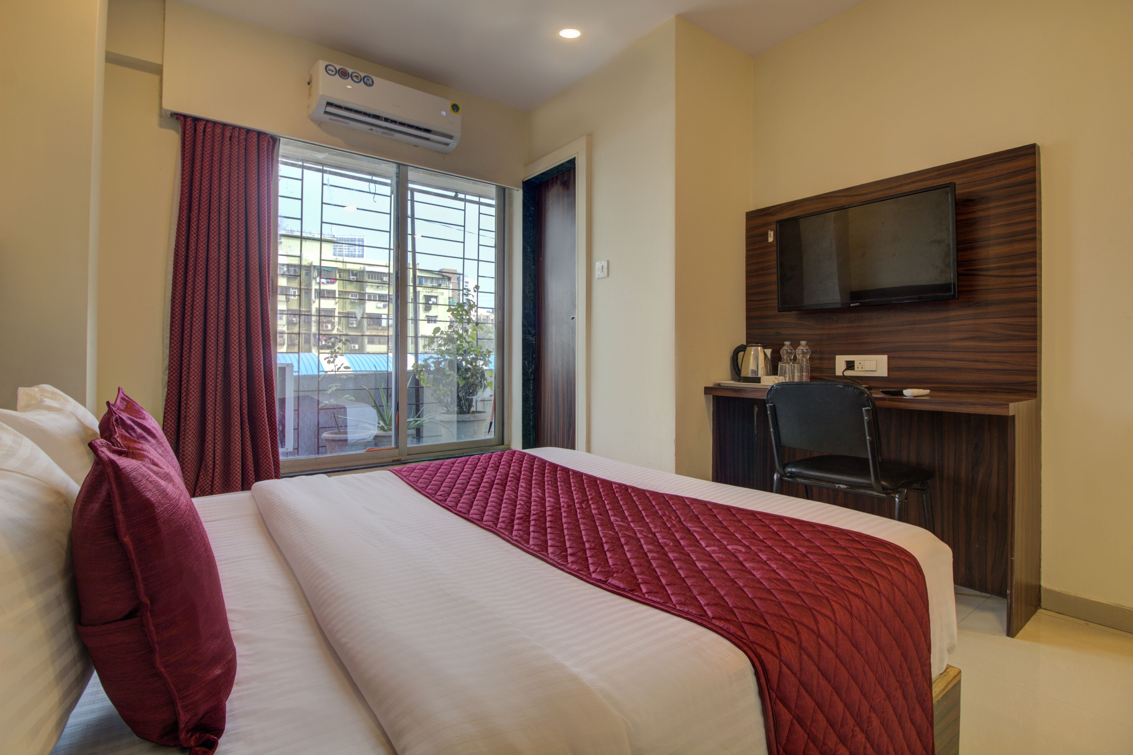 A hotel room with a large bed, a desk with a chair, a television mounted on the wall, and a window with curtains.