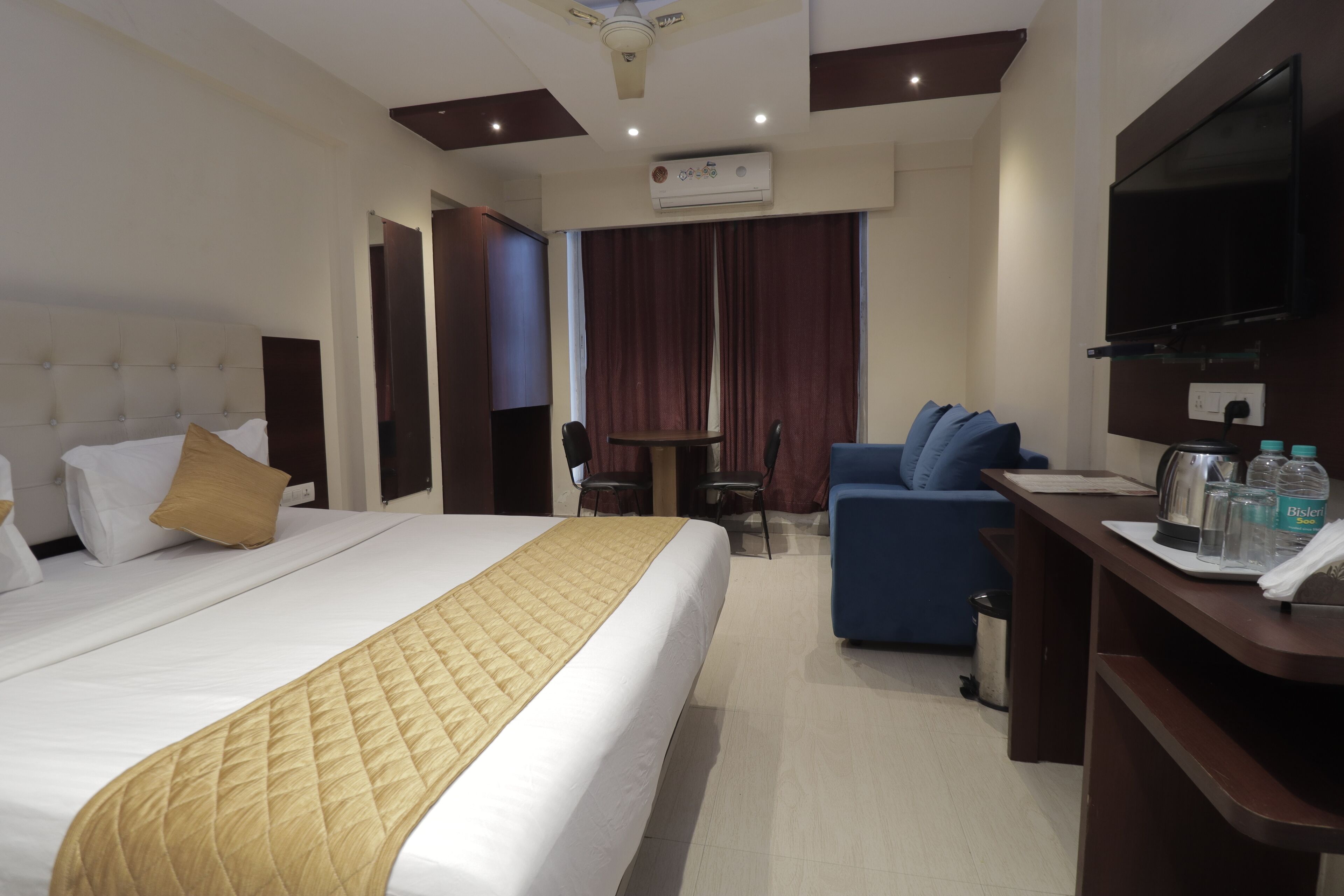 A hotel room with a bed, a desk, a chair, a TV, and a minibar.