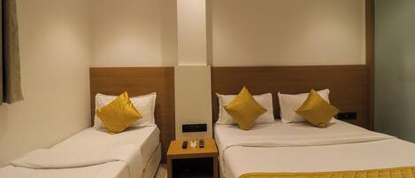A hotel room with two single beds, each with a wooden headboard, white bedding, and a yellow quilted throw. There is a small wooden nightstand between the beds with a remote control and a phone on it.