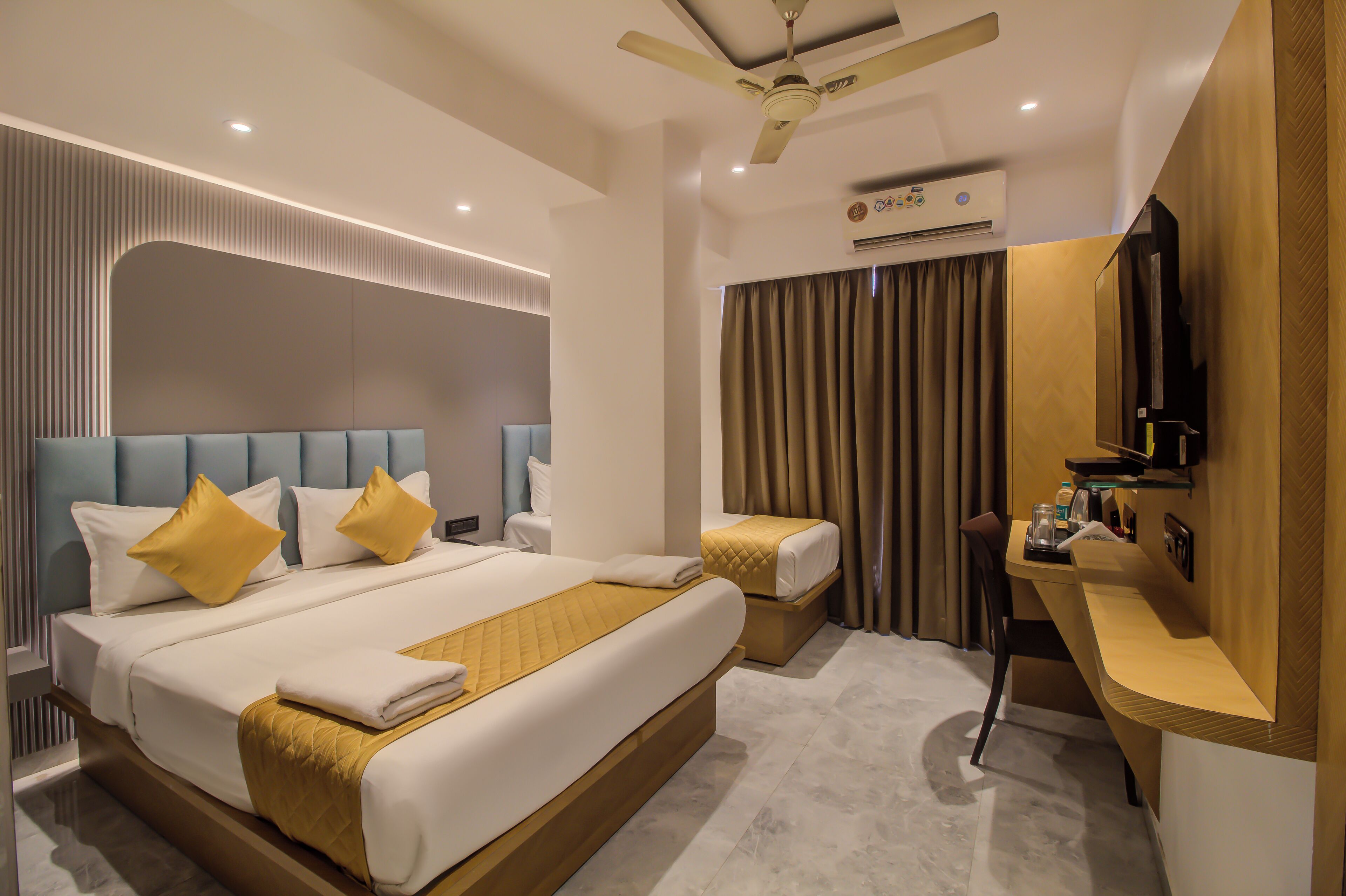 A modern hotel room with a large bed, a desk, a television, and an air conditioning unit.