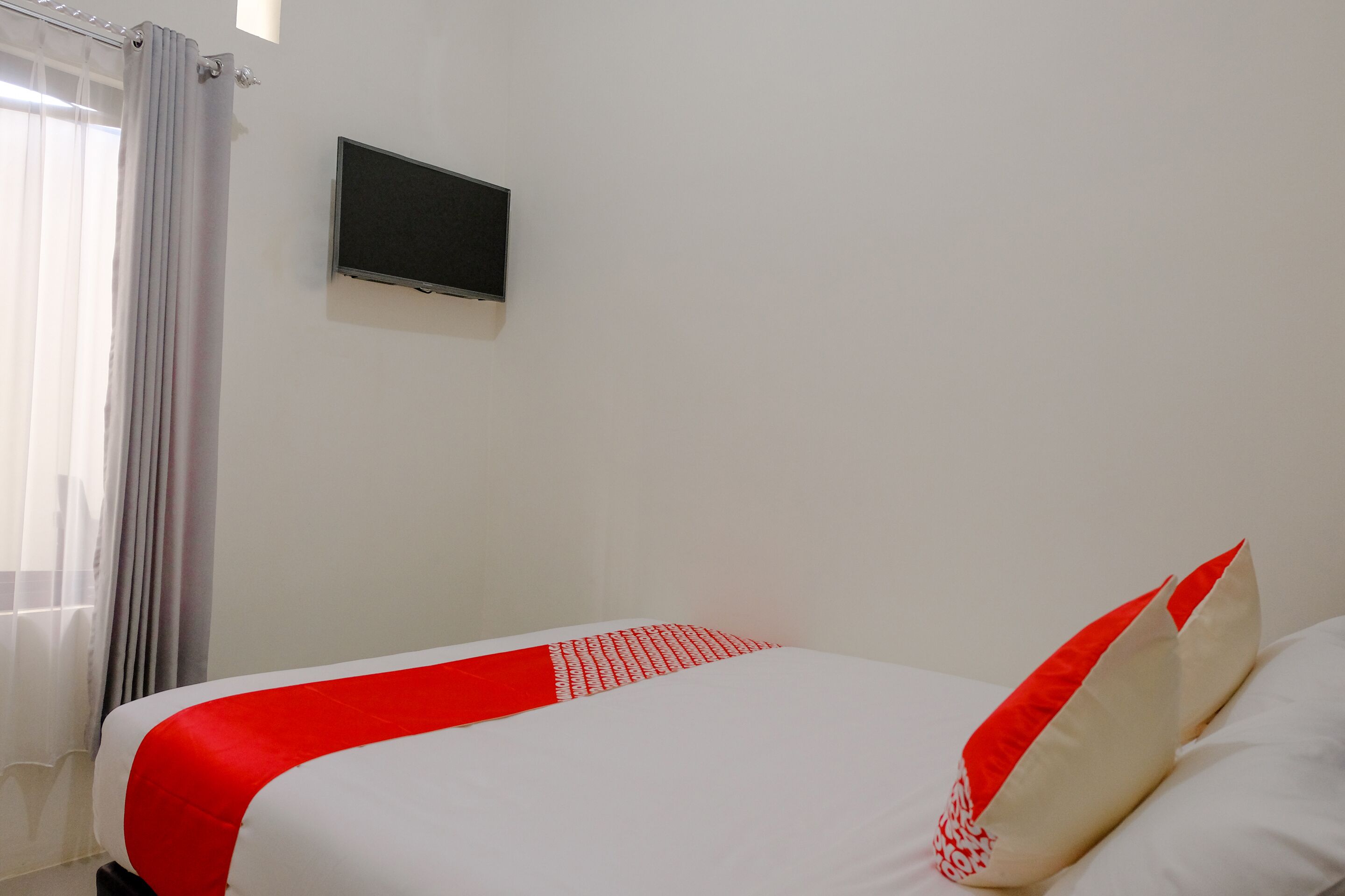 A hotel room with a bed, a flat-screen TV mounted on the wall, and a window with curtains.