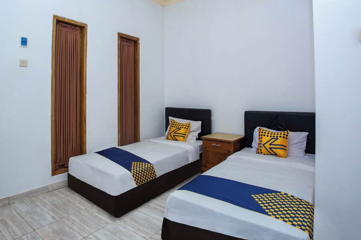 A hotel room with two single beds, each with a wooden headboard, a small wooden nightstand, and a window with brown curtains.