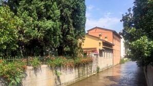 A narrow canal with a building on one side and a fence with flowers on the other. - Cosy apartment for 4 guests with WIFI, pool, TV, patio and pets allowed (Beati Bassi)