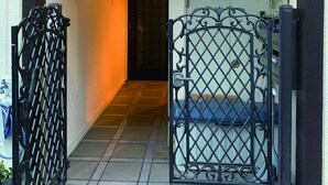 Entrada de un edificio con una verja metálica, una escalera que conduce al interior y una puerta con un cartel de número.