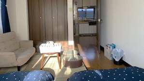 Un espacio habitable compacto con sofá, una mesita, una puerta de madera y una kitchenette visible a través de un acceso abierto.
