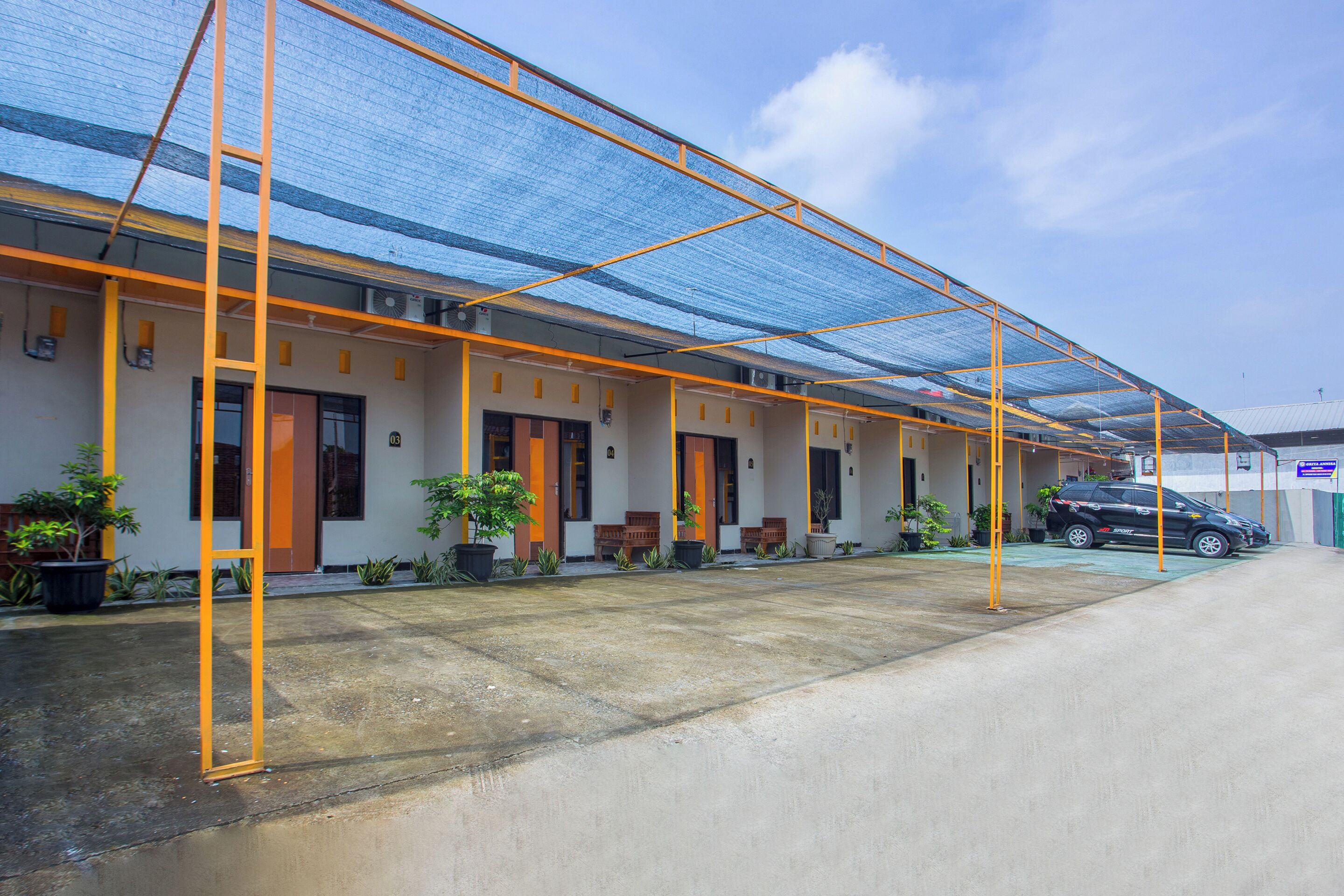 A building with a covered outdoor area, potted plants, and a parked car.