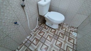 A bathroom with a white toilet, a shower hose, and patterned floor tiles. - Hotel O Griya Annisa (Tegal)
