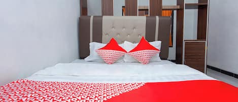 A bed with a white and red patterned bedspread, two red heart-shaped pillows, and a tufted headboard.