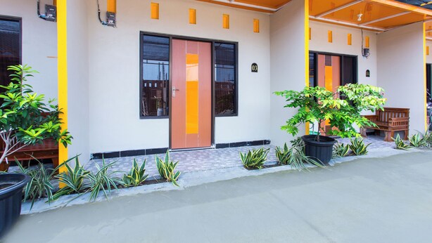 A building with a modern design, featuring a large entrance with a glass door, potted plants, and a small seating area. - Hotel O Griya Annisa (Tegal)