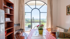 A dining area with a table set for two, a bookshelf, and a view through a large arched window. - Nice apartment in villa for 6 people with pool, A/C, WIFI, terrace and pets allowed (Azzano D'asti)