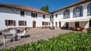 A courtyard with a white building, stone flooring, and outdoor seating. - Nice apartment in villa for 6 people with pool, A/C, WIFI, terrace and pets allowed (Azzano D'asti)