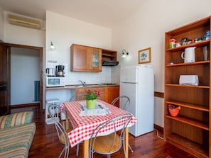 A compact kitchen with wooden cabinets, a white refrigerator, and a dining table with a checkered tablecloth. - Lovely apartment in villa for 6 guests with pool, A/C, WIFI, terrace and pets allowed (Azzano D'asti)