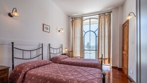 A bedroom with two beds, a wooden floor, a window with curtains, and wall-mounted lights. - Nice apartment in villa for 6 people with pool, A/C, WIFI, terrace and pets allowed (Azzano D'asti)