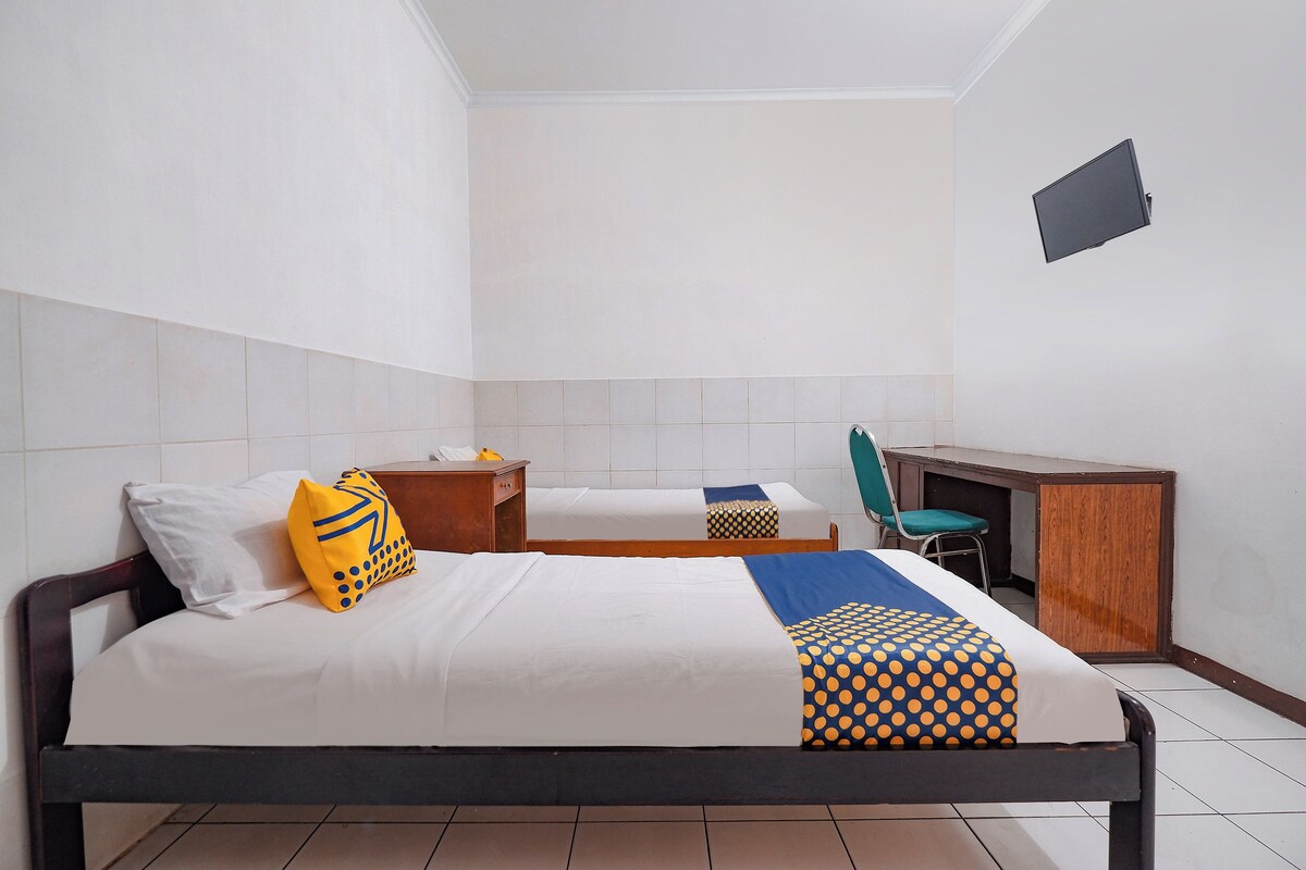 A hotel room with two beds, a desk, a chair, and a TV mounted on the wall.