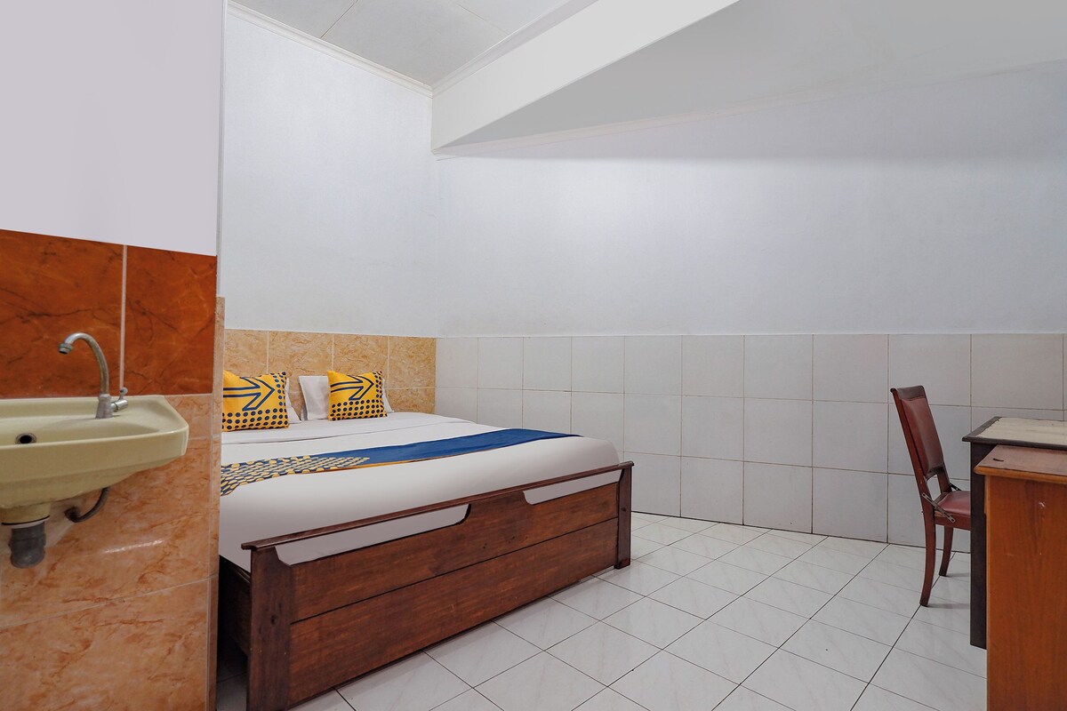 A bedroom with a bed, a wooden desk, a chair, and a sink.