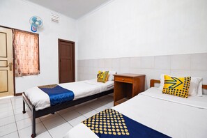 A room with two single beds, a wooden nightstand, a small table, a fan, and a door. - Hotel O Sartika Inn Pati (Pati)
