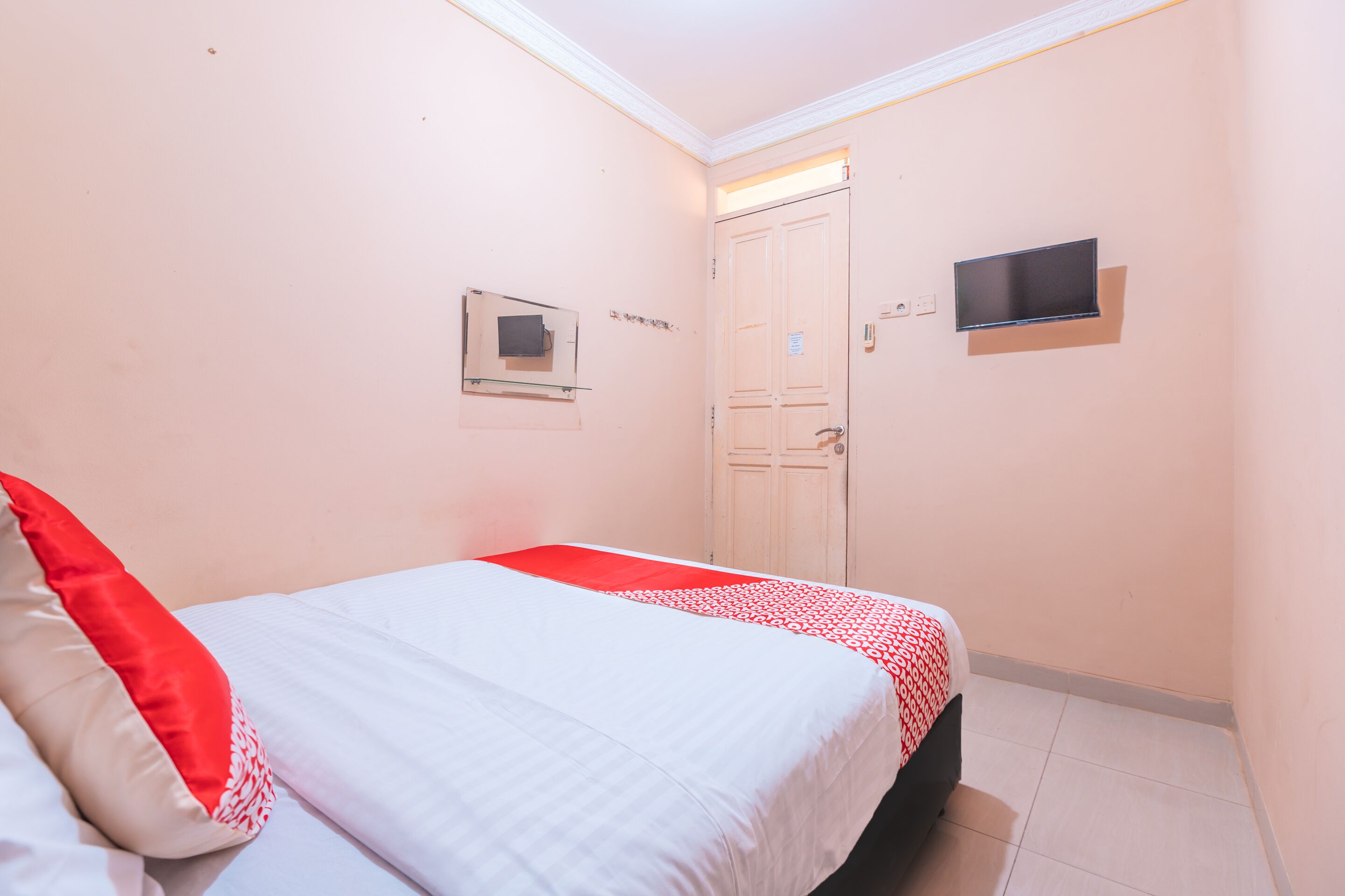 Un dormitorio con una cama, televisor montado en la pared y una puerta.