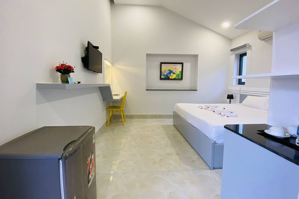 A compact hotel room with a bed, a desk, a chair, a TV, and a refrigerator.