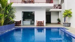 Ein zweistöckiges Gebäude mit Swimmingpool, einem Balkon mit Holzgeländer und Kübelpflanzen.