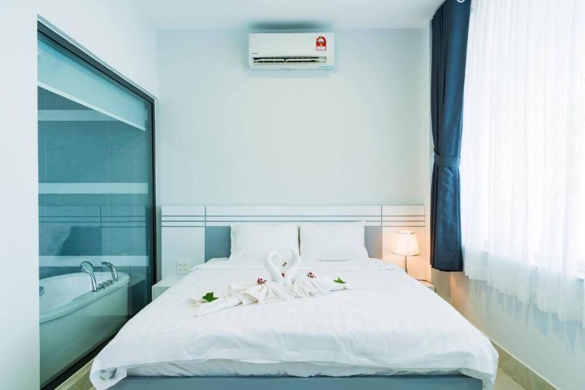 A hotel room with a bed, a window with a view, a wall-mounted air conditioner, and a bedside lamp.